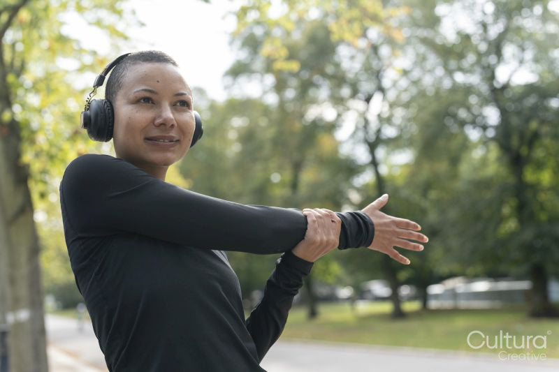 Woman in headphones and sports clothing stretching arm in park