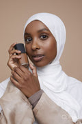 Studio portrait of young woman in white hijab holding foundation bottle
