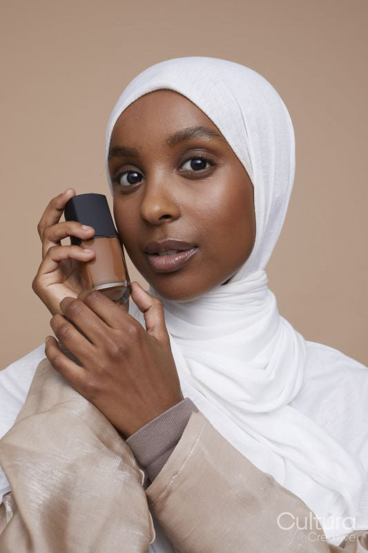 Studio portrait of young woman in white hijab holding foundation bottle