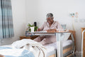 Smiling senior woman in bathrobe sitting on bed and doing crossword puzzle in nursing home