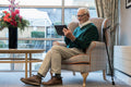Senior man sitting in armchair and using tablet in nursing home