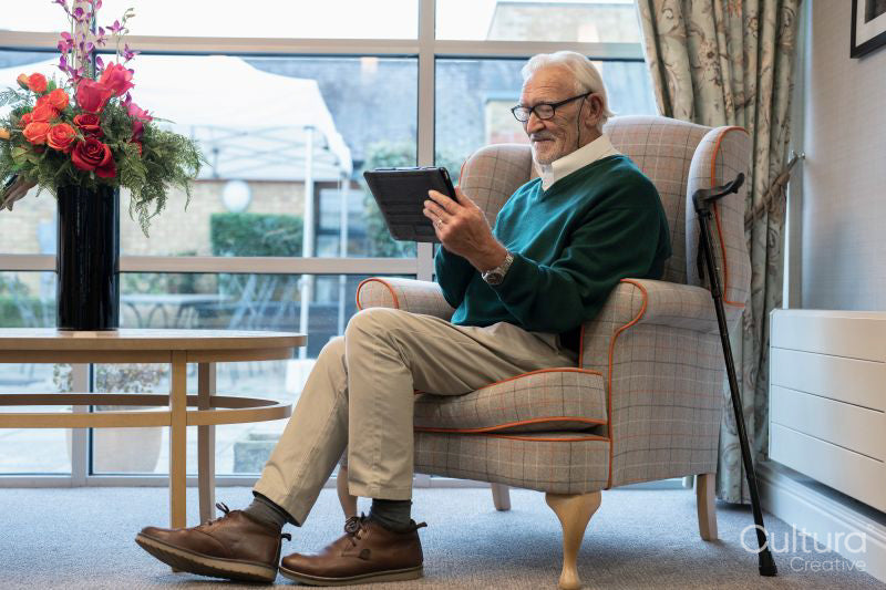 Senior man sitting in armchair and using tablet in nursing home