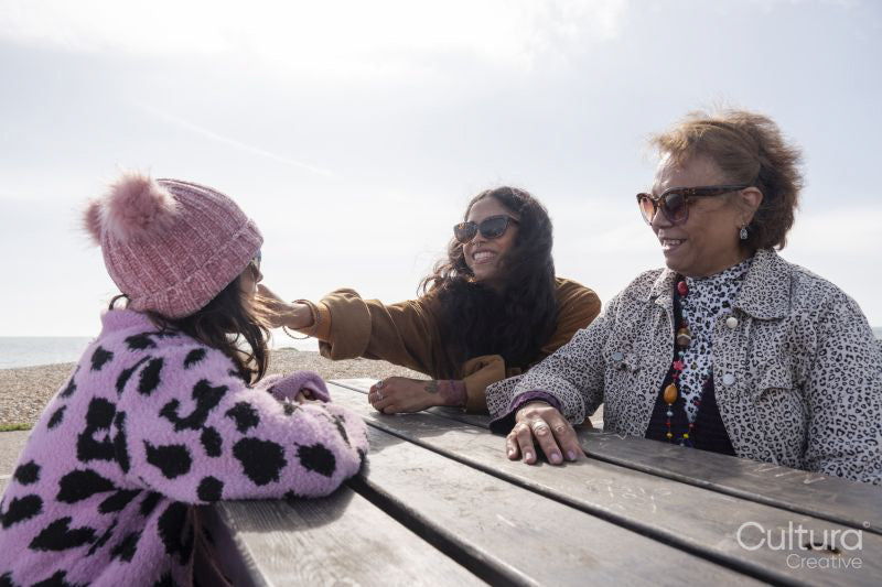 Grandmother, mother and daughter resting by picnic table on beach