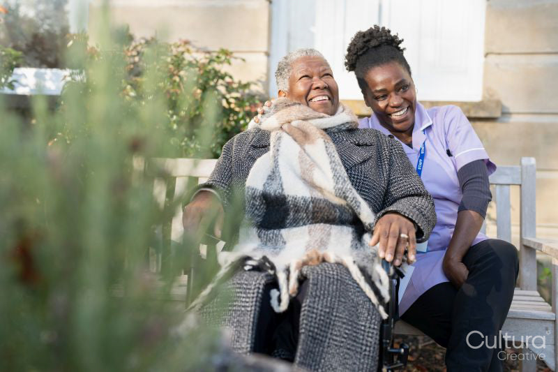 Smiling nurse and senior woman in wheelchair relaxing in park