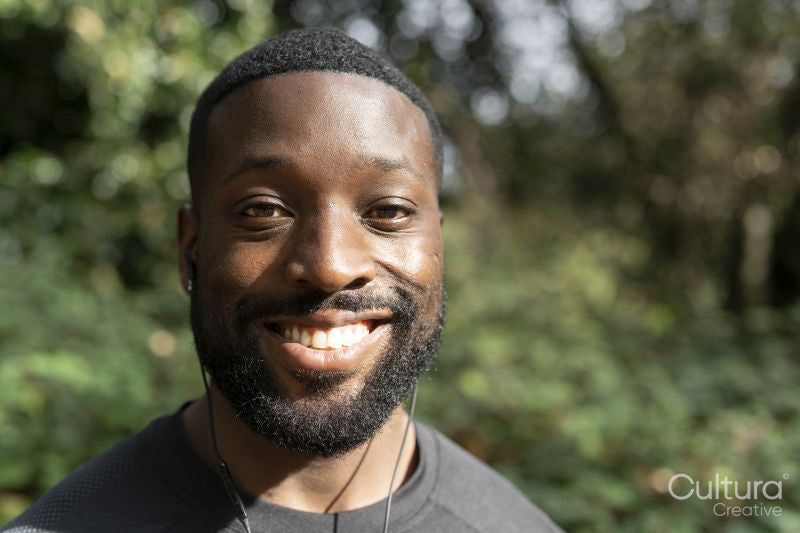 Portrait of smiling man with earbuds standing in park