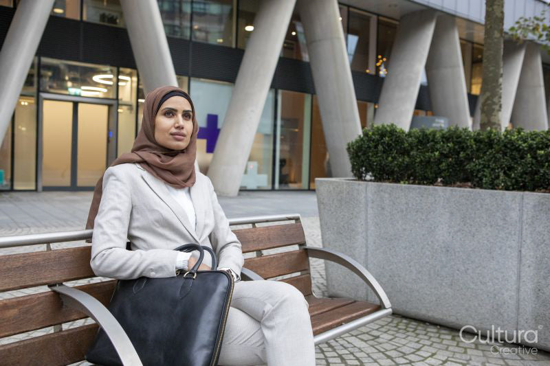 Woman in business clothing and hijab sitting on bench