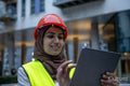Female engineer in hijab and hardhat using digital tablet