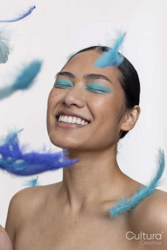 Blue feathers falling in front of smiling woman with closed eyes