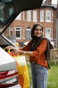 Woman wearing hijab putting shopping bags into car trunk