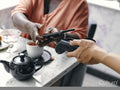 Close-up of woman paying with smart phone at cafe table