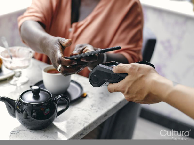Close-up of woman paying with smart phone at cafe table