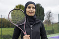 Portrait of woman in black sports clothing and hijab holding tennis racket