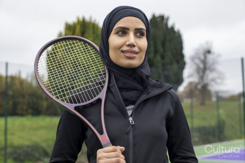 Portrait of woman in black sports clothing and hijab holding tennis racket
