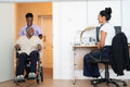 Smiling female nurse with senior woman sitting in wheelchair entering doctors office