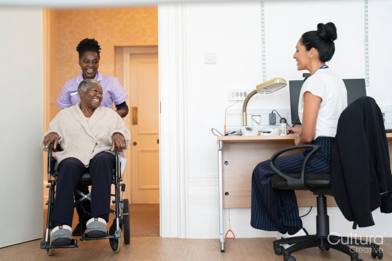 Smiling female nurse with senior woman sitting in wheelchair entering doctors office