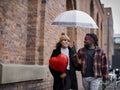 Couple with heart shaped balloon and umbrella walking on sidewalk