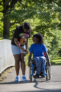 Teenage girl in wheelchair with friend walking in park
