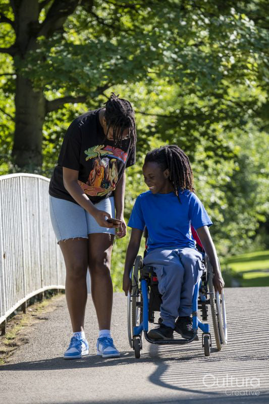 Teenage girl in wheelchair with friend walking in park
