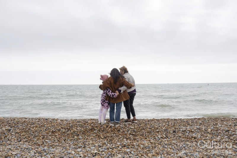 Grandmother, mother and daughter embracing on beach on cloudy day