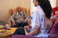 Smiling senior man sitting in armchair and looking at nurse