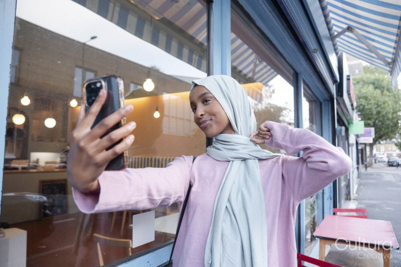 Young woman in hijab taking selfie in front of cafe