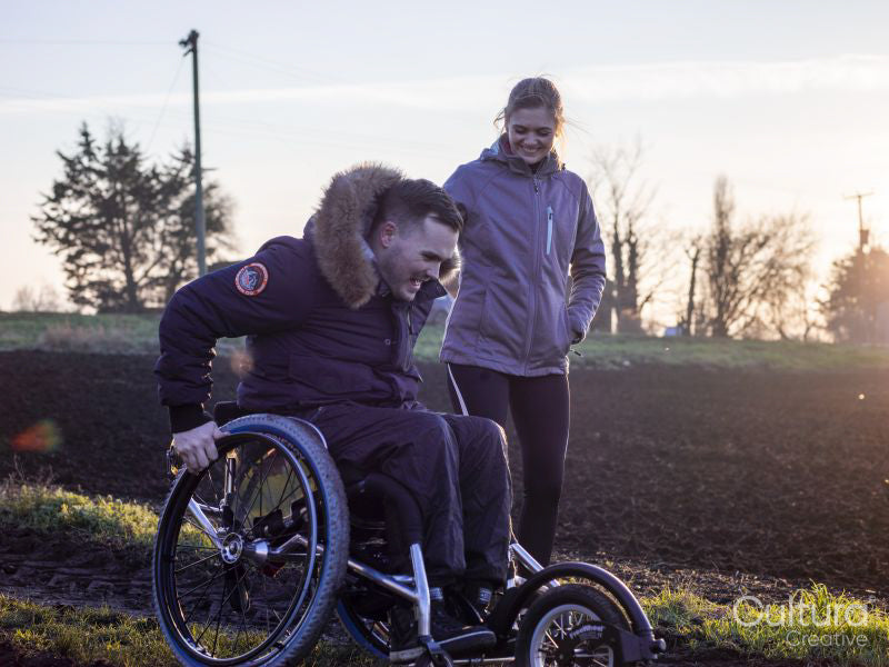 Smiling woman and man on wheelchair in field