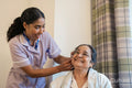 Nurse helps senior lady putting on hearing aid at nursing home