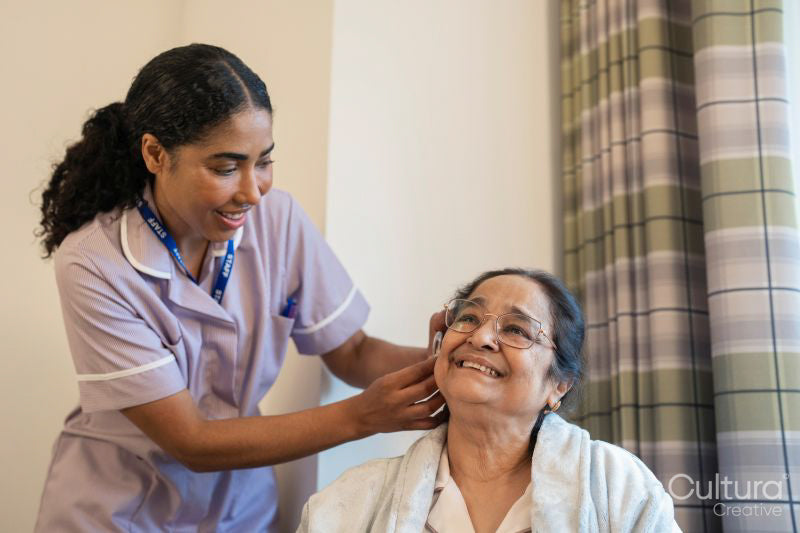 Nurse helps senior lady putting on hearing aid at nursing home
