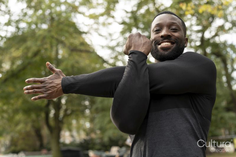 Portrait of smiling athletic man stretching arm in park