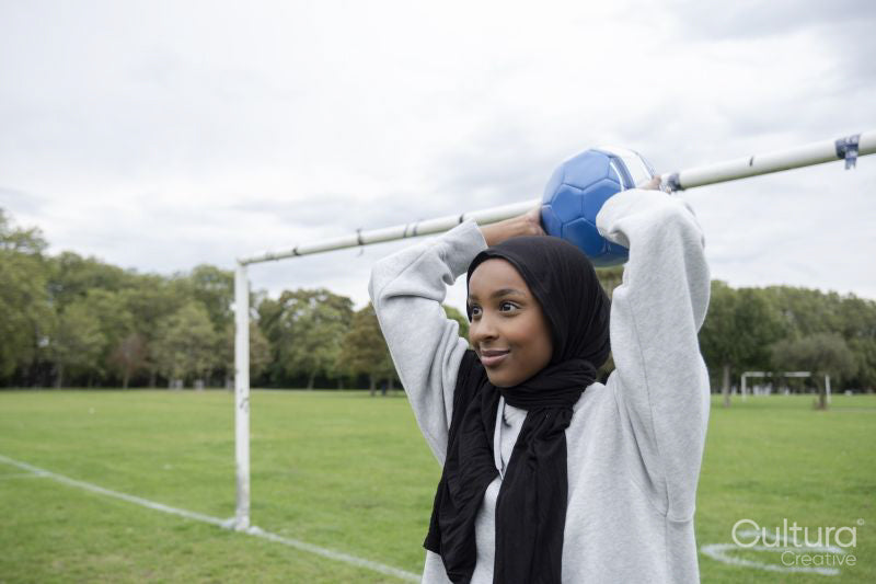 Smiling woman in hijab throwing soccer ball in park