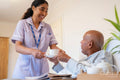 Nurse serving coffee to senior man lying in bed in room at nursing home