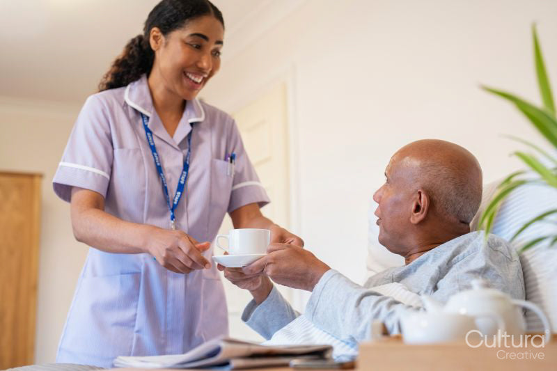Nurse serving coffee to senior man lying in bed in room at nursing home
