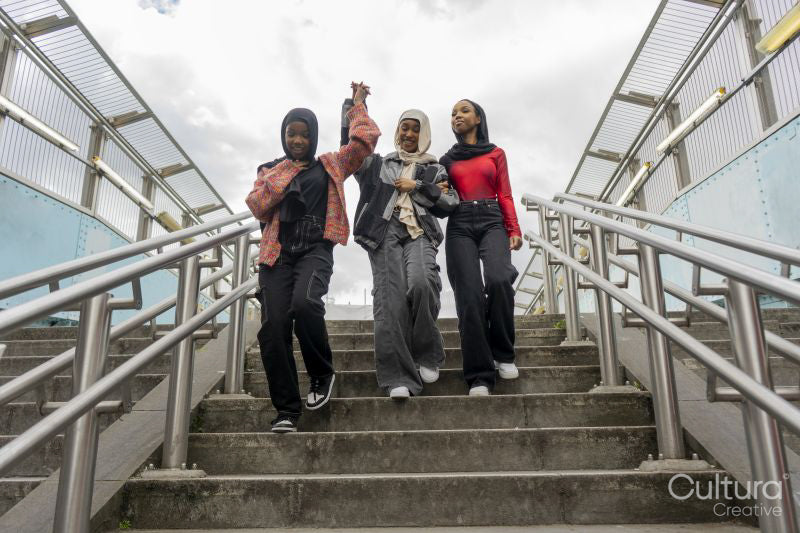 Smiling young women wearing hijabs holding hands on steps