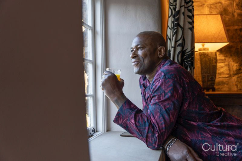 Man leaning on window sill with glass of juice and looking out window