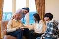 Adult daughter, grandson and care giver looking at smiling senior man during visiting in nursing home