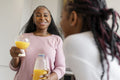 Woman drinking orange juice while chatting with girlfriend in kitchen