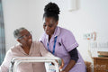Caregiver assisting smiling senior woman sitting on bed and holding mobility walker