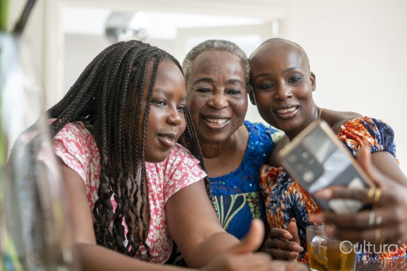 Smiling teenage girl with mother and grandmother taking selfie at table