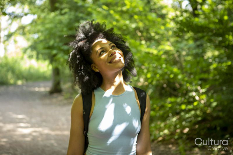 Young woman hiking in forest, looking up at trees