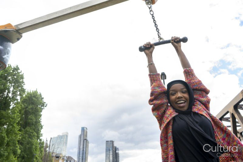 Portrait of smiling woman wearing hijab hanging on exercise machine in park