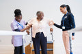 Female therapist and nurse assisting senior woman descending steps in exercise room
