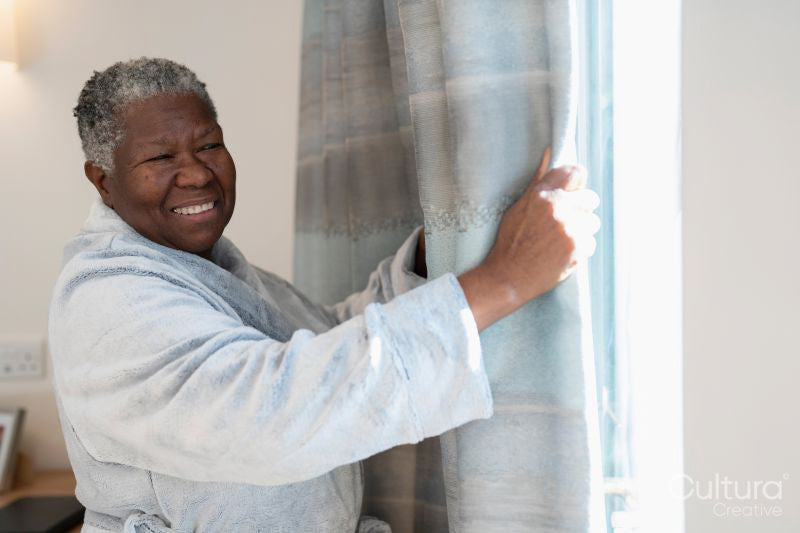 Smiling senior woman in bathrobe standing by window