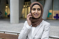 Woman in hijab sitting on bench and talking on smart phone