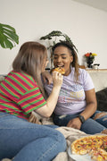 Two young women sitting on sofa and eating pizza