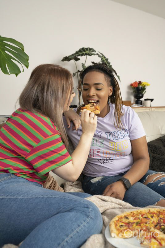 Two young women sitting on sofa and eating pizza