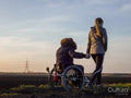 Rear view of woman and man on wheelchair in field at sunset