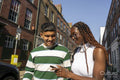 Smiling young friends using smart phone in city