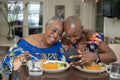 Smiling woman with adult daughter eating dinner and looking at smart phone