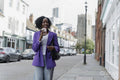 Smiling woman walking and drinking coffee on sidewalk