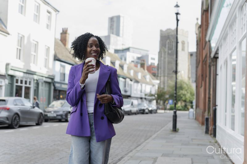 Smiling woman walking and drinking coffee on sidewalk
